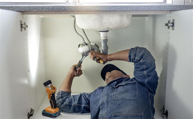 Plumber repairing pipes beneath a bathroom sink in Orlando