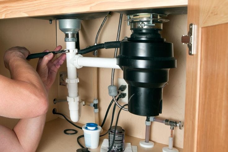 Plumber installing a garbage disposal beneath a kitchen sink in Orlando