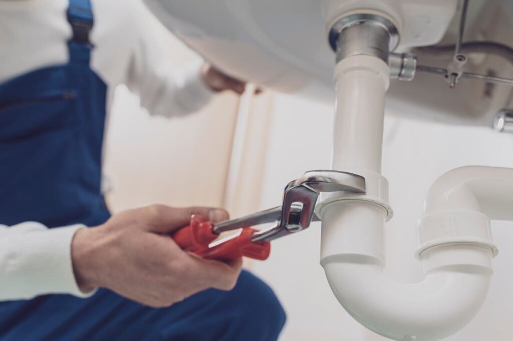 Plumber repairing a white drain pipe beneath a sink in Orlando